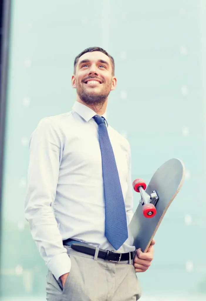 Jeune homme souriant en costume cravate avec un skate sous le bras